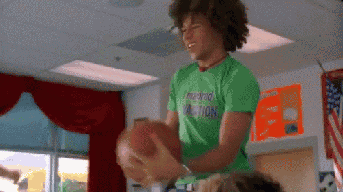 a young man in a green shirt is holding a football in a classroom .