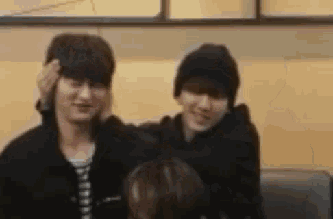 two young men are sitting next to each other on a couch and one of them is touching the other 's head .