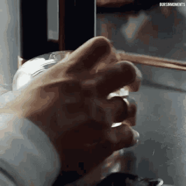 a close up of a person 's hand holding a glass of water with the words bursinmoments below it