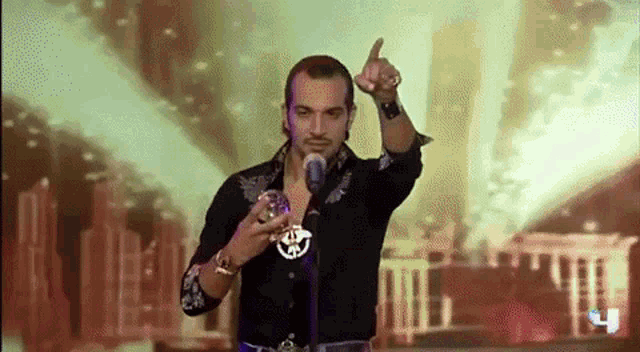 a man in a black shirt is singing into a microphone while holding a glass