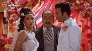 a bride and groom are standing next to each other in front of a floral backdrop .