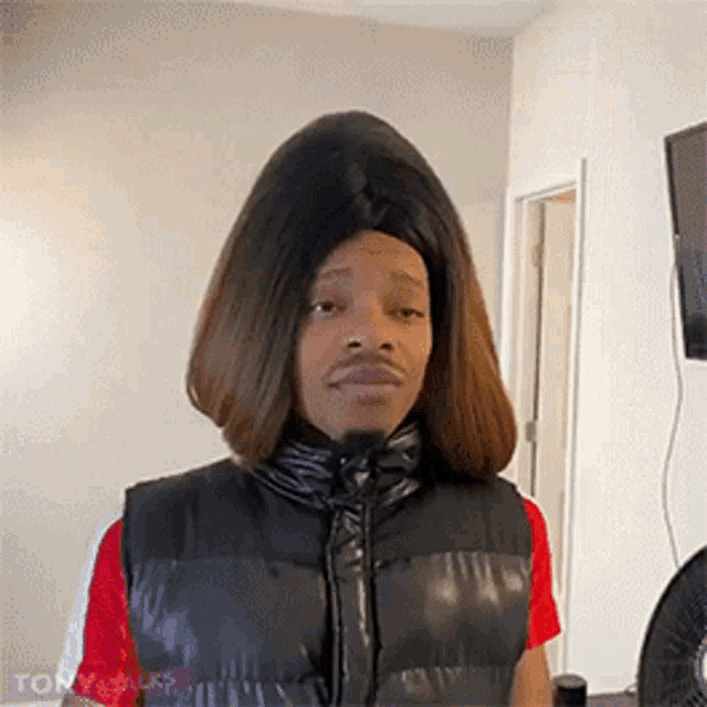 a man wearing a wig and a vest is standing in a living room .