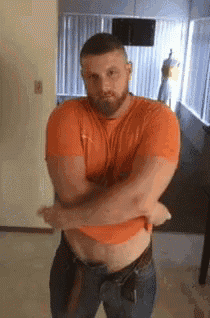 a man with a beard is standing in a room with his arms crossed and his shirt off .