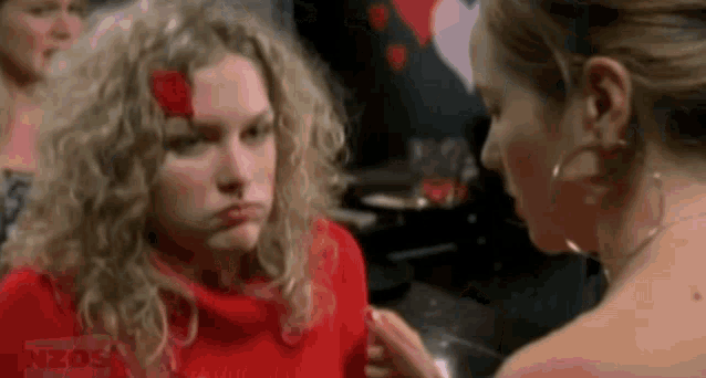 two women are standing next to each other in a room . one of the women has a red flower in her hair .