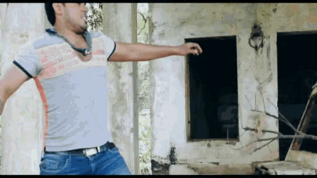 a man in a gray shirt and blue jeans is standing in front of a building