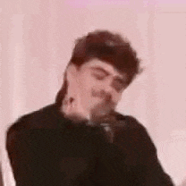 a man with a mullet is sitting in front of a microphone and making a funny face .