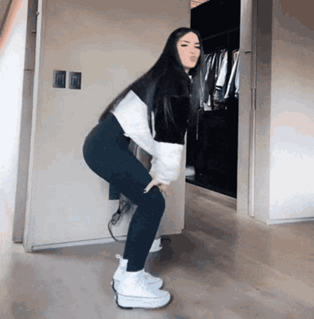 a woman in a black and white sweater and black leggings is standing on a wooden floor .