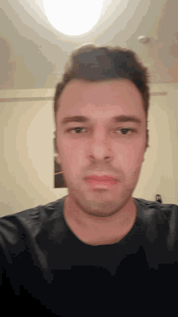 a man in a black shirt looks at the camera with a serious look on his face