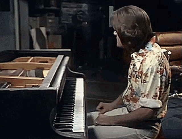 a man in a hawaiian shirt is sitting at a piano