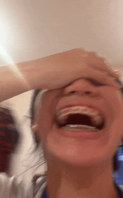 a woman with braces on her teeth is laughing and covering her face .