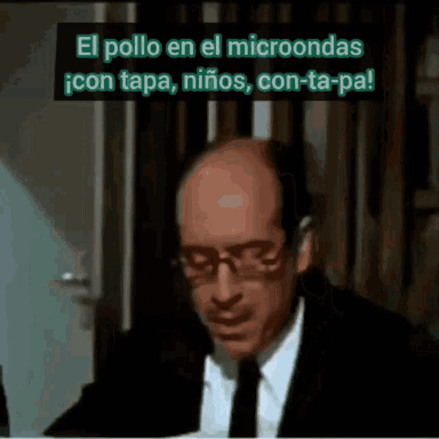 a man in a suit and tie is sitting in front of a sign that says el pollo en el microondas