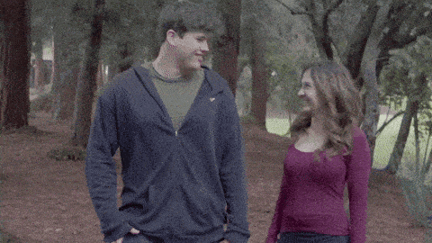 a man and a woman are walking in the woods and the man is wearing a nike hoodie