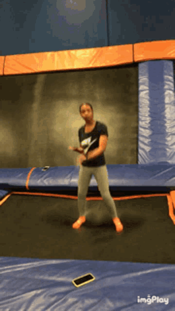 a woman in a nike shirt is jumping on a trampoline with a cell phone in the foreground