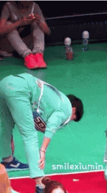 a man in a green jumpsuit is bending over on a green floor with smilexiumin written on the bottom right