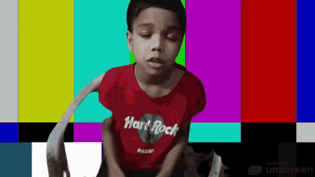 a young boy wearing a red hard rock shirt sits in a chair