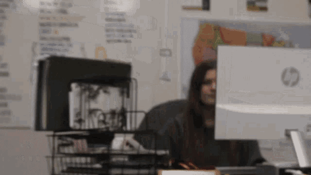 a woman is sitting at a desk in front of an hp computer