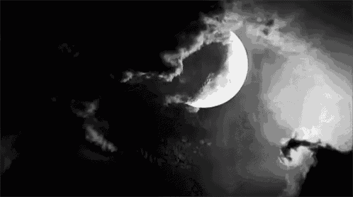 a black and white photo of a crescent moon surrounded by clouds in the night sky .