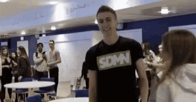 a man wearing a sdmn t-shirt is standing in front of a woman .