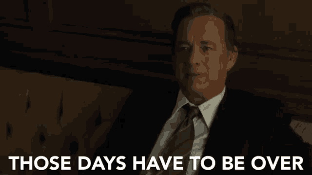 a man in a suit and tie sits on a couch with the words " those days have to be over " behind him