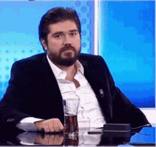 a man in a suit sits at a table with a glass of beer