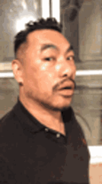 a man with a mustache is wearing a black shirt and looking at the camera .