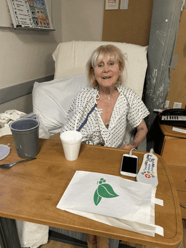 an older woman in a hospital gown sits at a table
