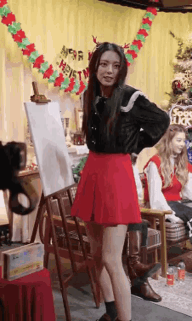 a woman in a red skirt is standing in front of an easel in a room decorated for christmas .