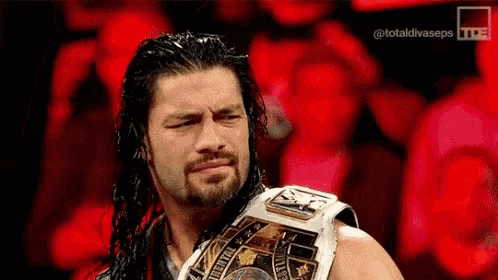 roman reigns is wearing a world heavyweight wrestling championship belt and making a funny face .