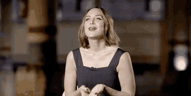 a woman in a black dress is talking into a microphone while standing in a dark room .