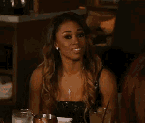 a woman in a black dress is sitting at a table with a drink in her hand