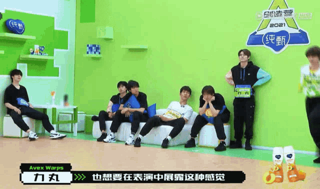 a group of young men are sitting on a couch in front of a green wall that says avex wars on it