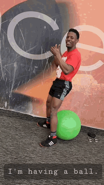 a man standing next to a green ball that says i 'm having a ball on the bottom