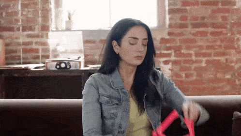 a woman in a denim jacket is sitting on a couch in front of a brick wall .