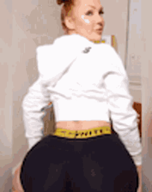 a woman in a white hoodie and black shorts is standing in a room .