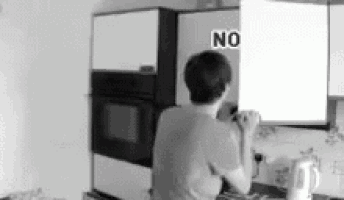 a black and white photo of a man in a kitchen with a sign that says no on it