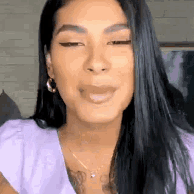 a woman with long black hair is wearing a purple shirt and earrings and smiling .