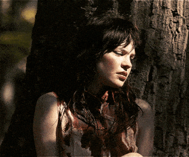 a woman leaning against a tree with a dirty shirt on
