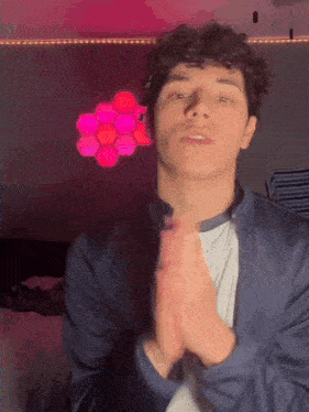 a young man with curly hair is clapping his hands in front of a pink background