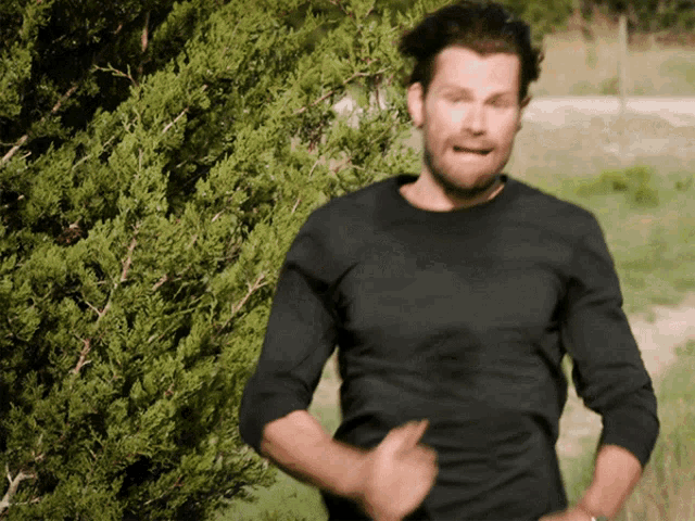 a man in a black shirt is standing in front of a bush