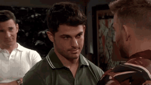 a man in a green polo shirt looks at another man in a striped shirt