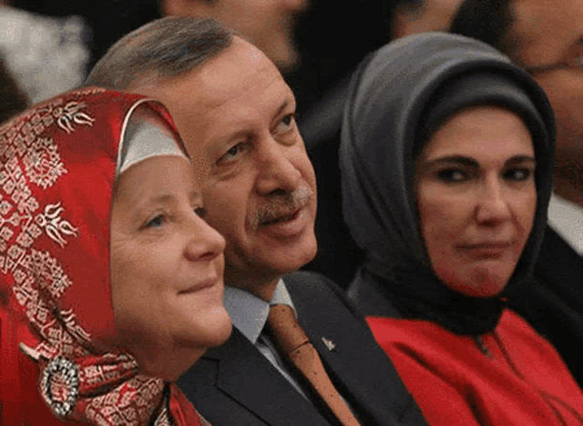 a man and two women are sitting next to each other and one of the women is wearing a red hijab