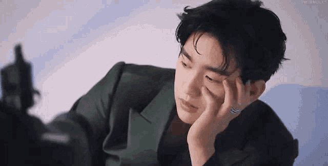 a young man in a green suit is sitting down with his hand on his forehead .