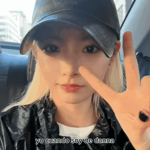 a woman wearing a black hat giving a peace sign with yo cuando soy de danna below her
