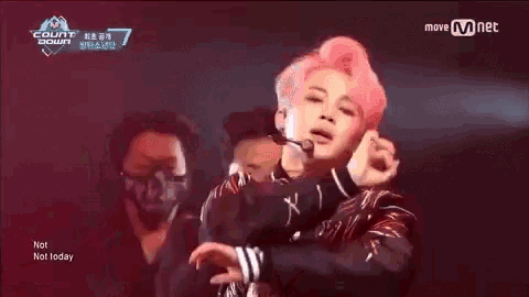 a person with pink hair is dancing on a stage in front of a group of people .