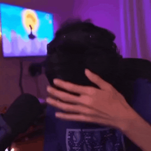 a person is covering their face with their hands in front of a television .