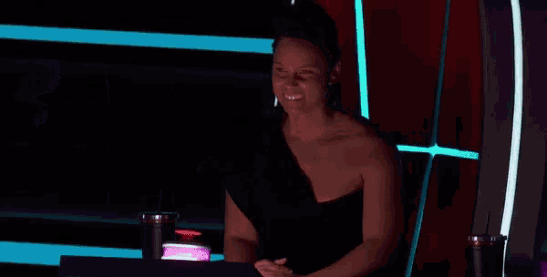 a woman in a black dress is sitting at a table in front of a purple light .