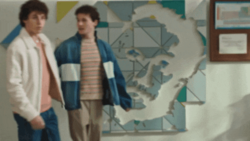 two men are standing in front of a wall with a map of the world on it