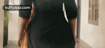 a woman in a black dress is walking down a hallway in a room .