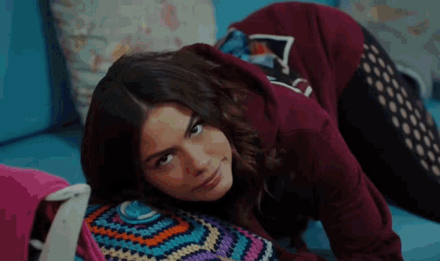 a woman in a burgundy hoodie is laying on her stomach on a blue couch