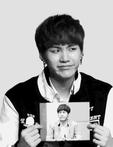 a young man is holding a picture of himself and the word ent is on the jacket he is wearing